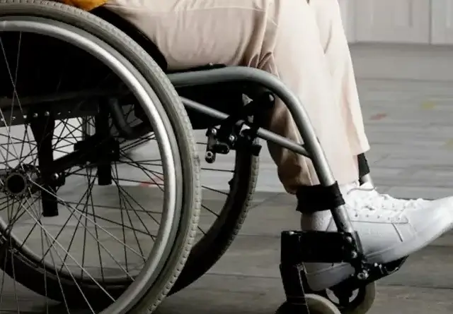 Person seated in a lightweight manual wheelchair showing large spoked rear wheel and footrest on indoor floor
