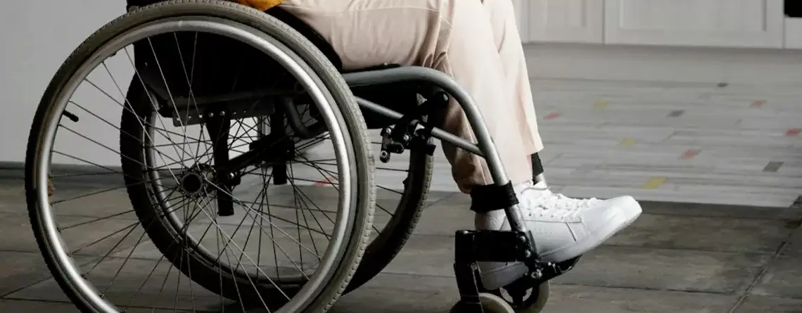 Person seated in a lightweight manual wheelchair showing large spoked rear wheel and footrest on indoor floor